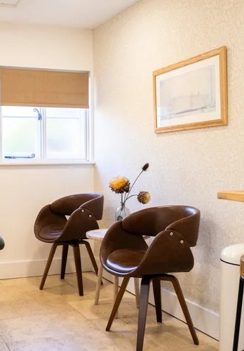 Two brown armchairs and a small table with dried flowers in a calm, light therapy room at Oak House