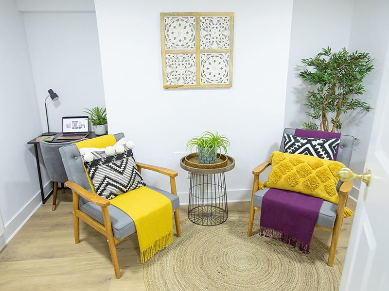 Two grey armchairs angled towards each other around a round rug in a calm, light-filled therapy room